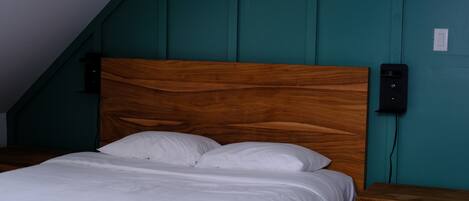 A bedroom with a wooden headboard, a white bedspread, and a teal wall.