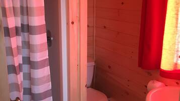 A wooden bathroom with a striped shower curtain, a white toilet, and a red-lit sink.