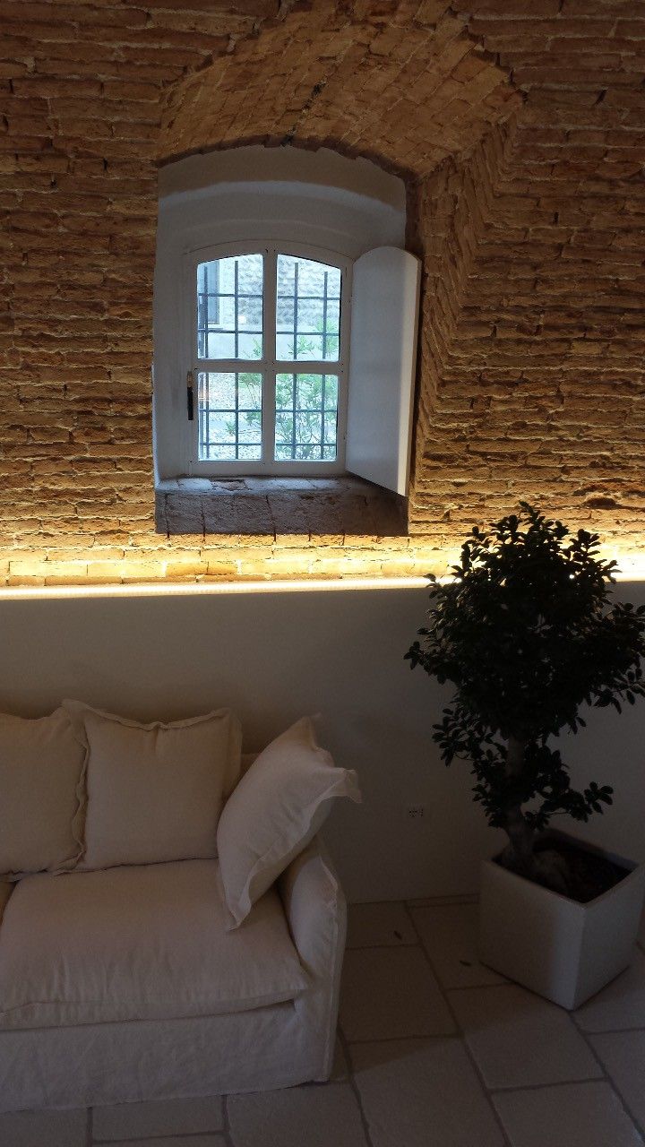 Ein Zimmer mit Backsteinwand, Fenster mit Blick, einem weißen Sofa und einem Blumentopf.