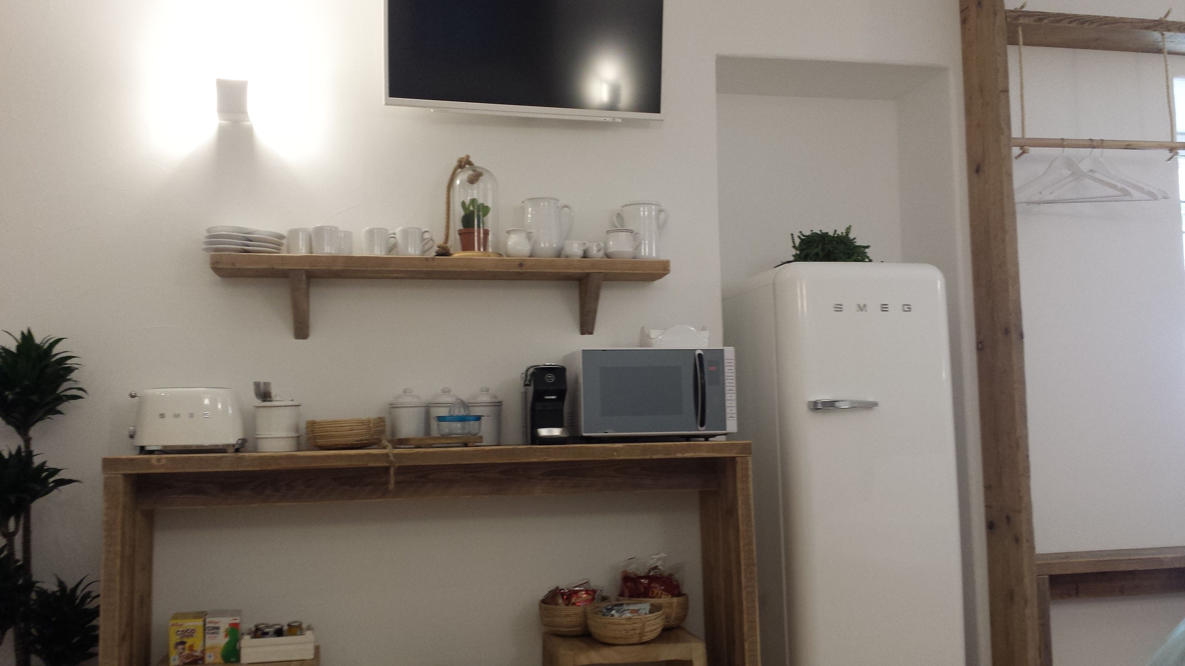 A kitchen with a microwave, coffee maker, and shelves with dishes and a potted plant.