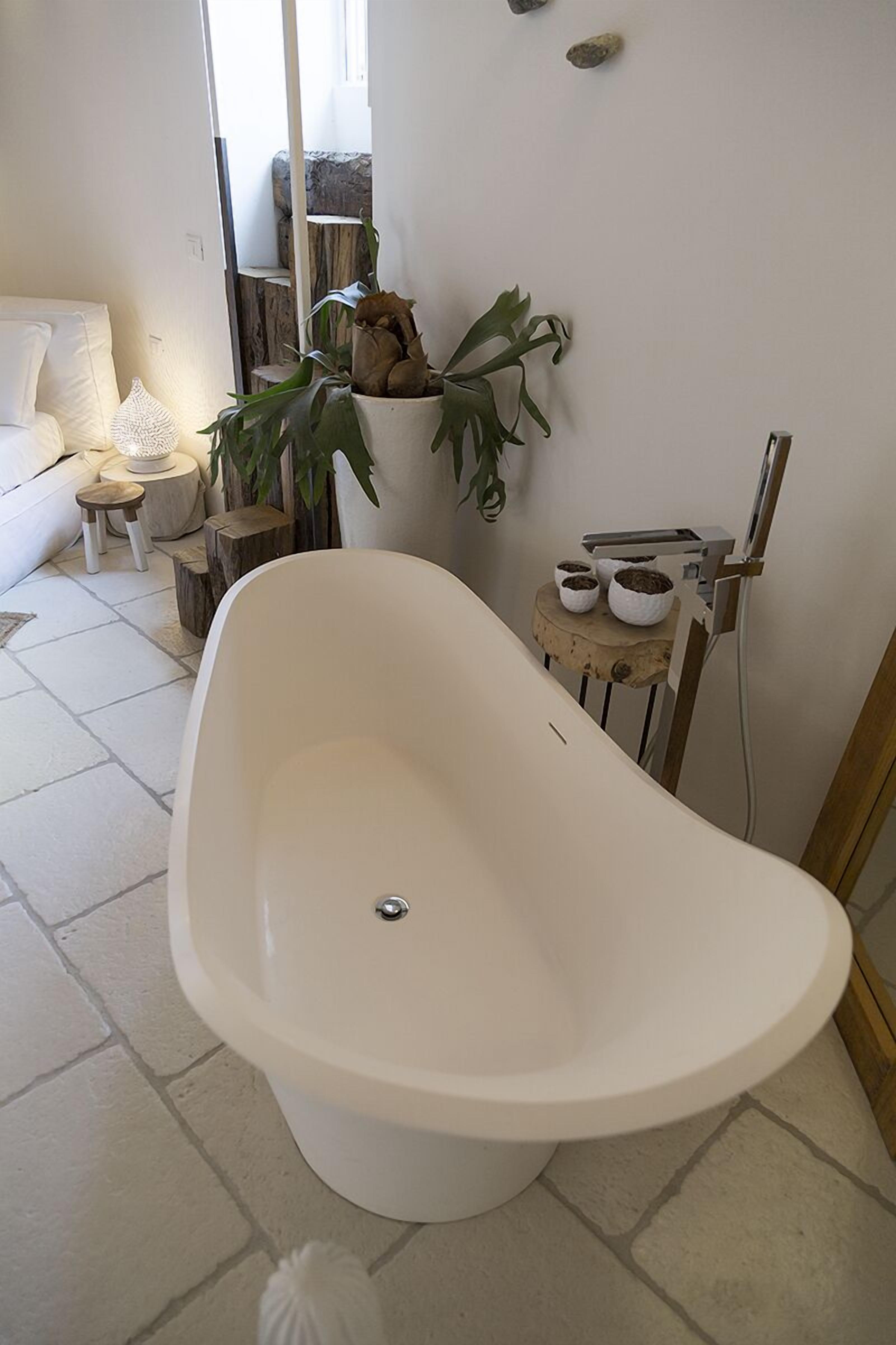 Un bagno moderno con una vasca freestanding, un piccolo sgabello di legno con una pianta e un lavandino bianco.