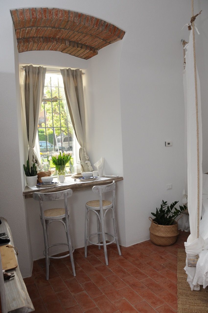 A corner room with a window, two white chairs, a small table, and a potted plant.