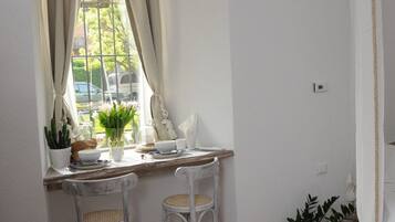 A corner room with a window, two white chairs, a small table, and a potted plant.
