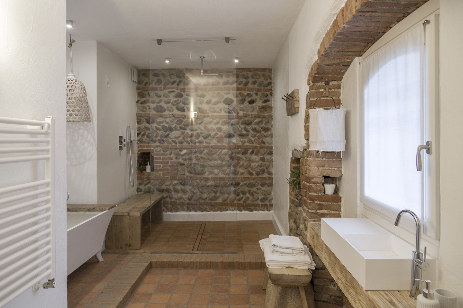 Une salle de bain avec un mur en pierre, une baignoire, une douche et un lavabo.