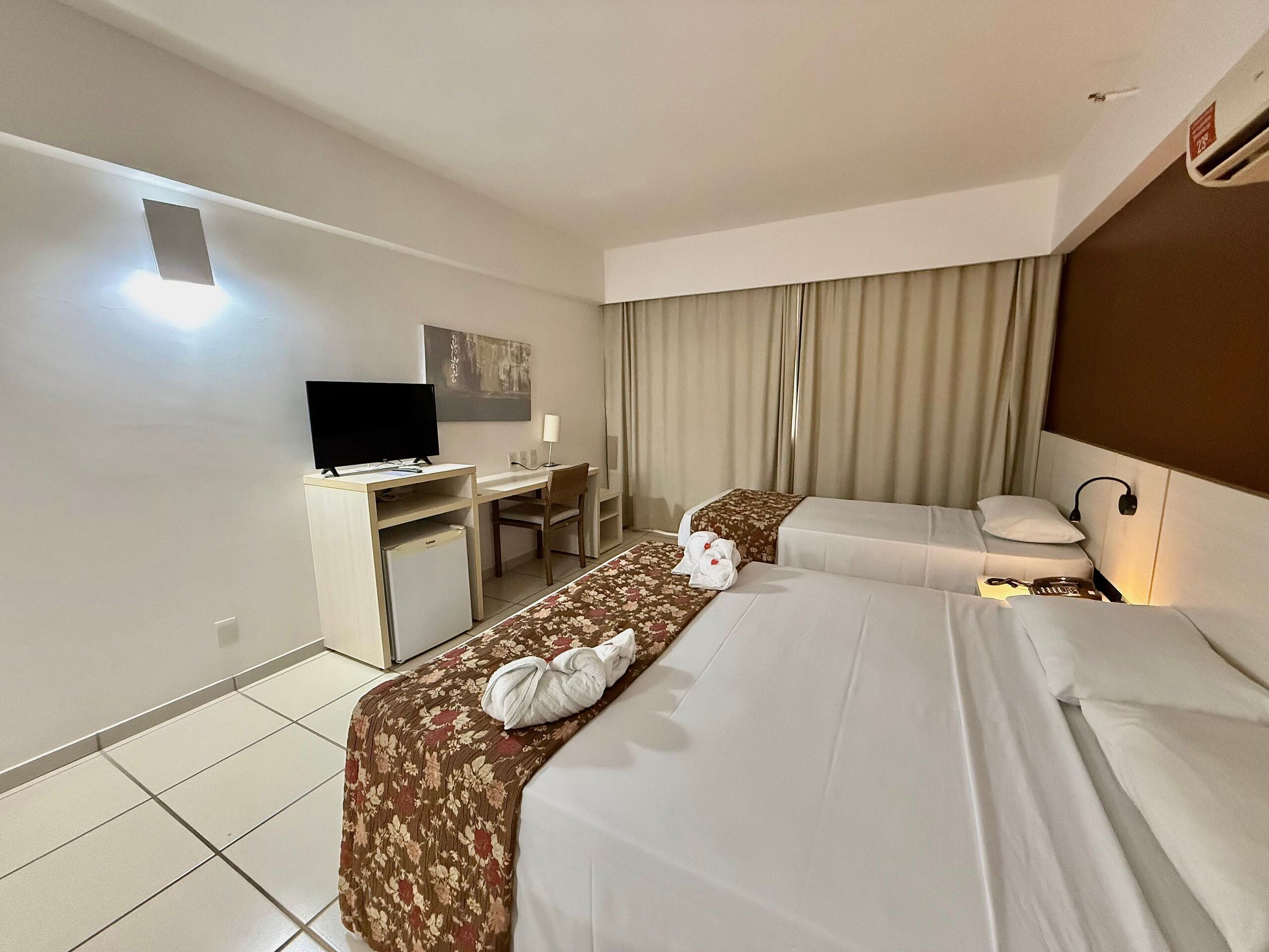 Ein Hotelzimmer mit Bett, Schreibtisch, Fernseher und einem Fenster mit Vorhängen.