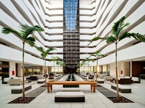 A spacious lobby with a central water feature, multiple seating areas, and tall palm trees. - Suite Le Jardin Via Caldas (Caldas Novas)