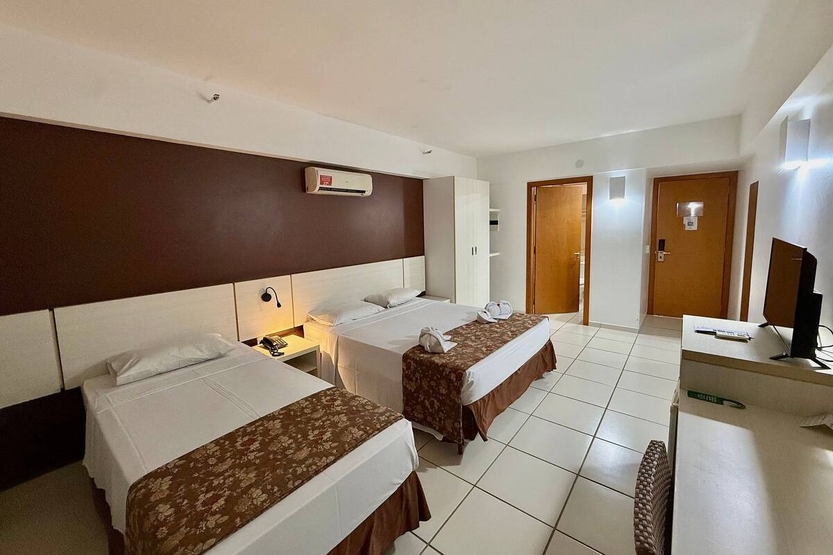 A hotel room with two beds, a desk with a computer, a TV, and a bathroom door.