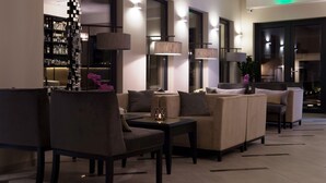 Un vestíbulo moderno con un sofá y sillones, una zona de bar con estanterías y lámparas de pie.