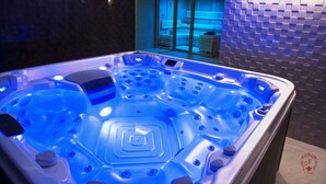 Un moderno spa con un amplio jacuzzi iluminado, una silla de masajes y una zona de relajación con paredes de vidrio.