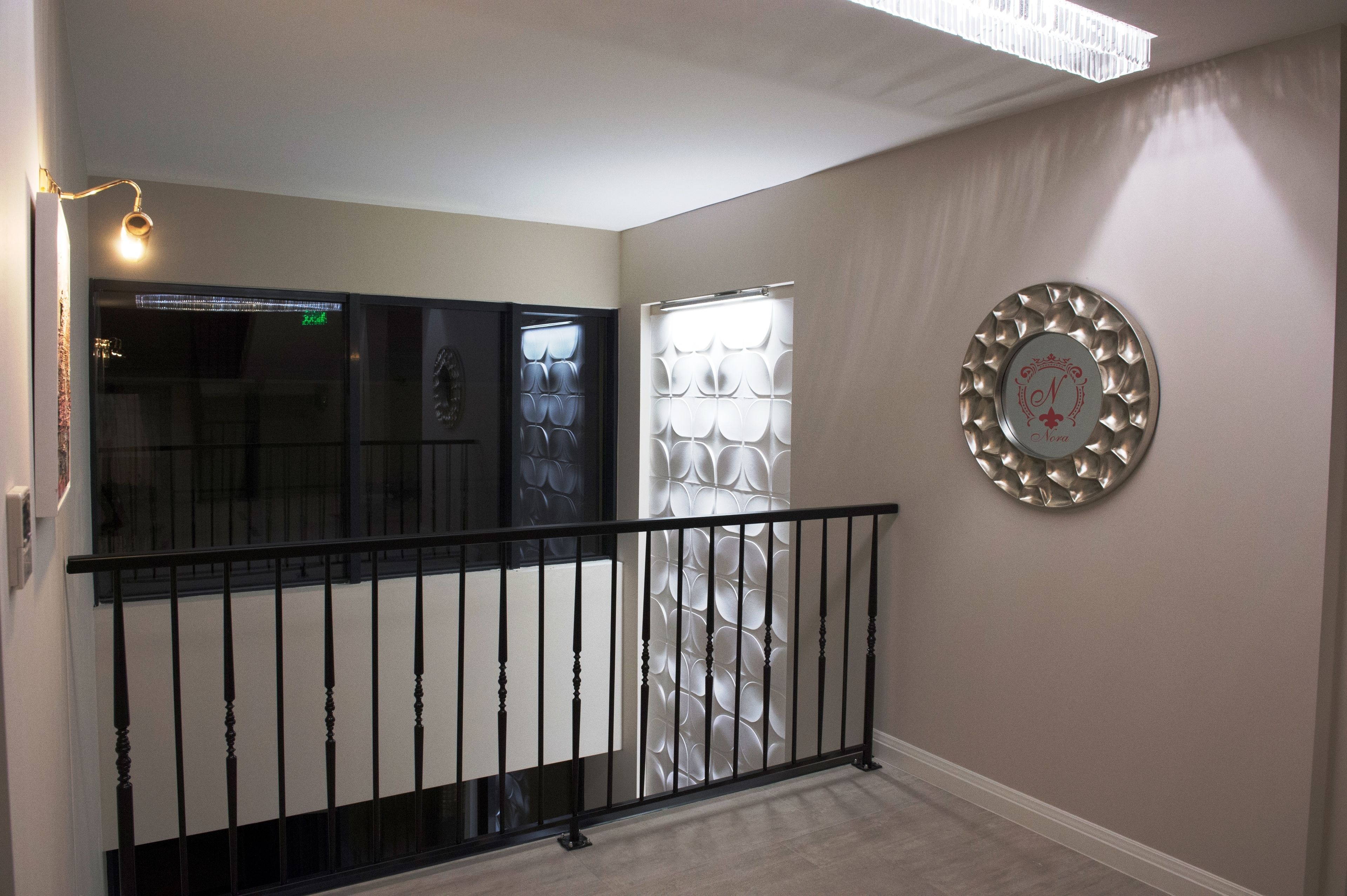 Um corredor com guarda-corpo preto, um painel decorativo na parede e um luminário.