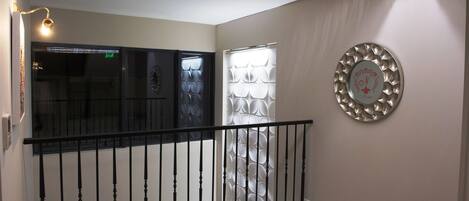 Um corredor com guarda-corpo preto, um painel decorativo na parede e um luminário.