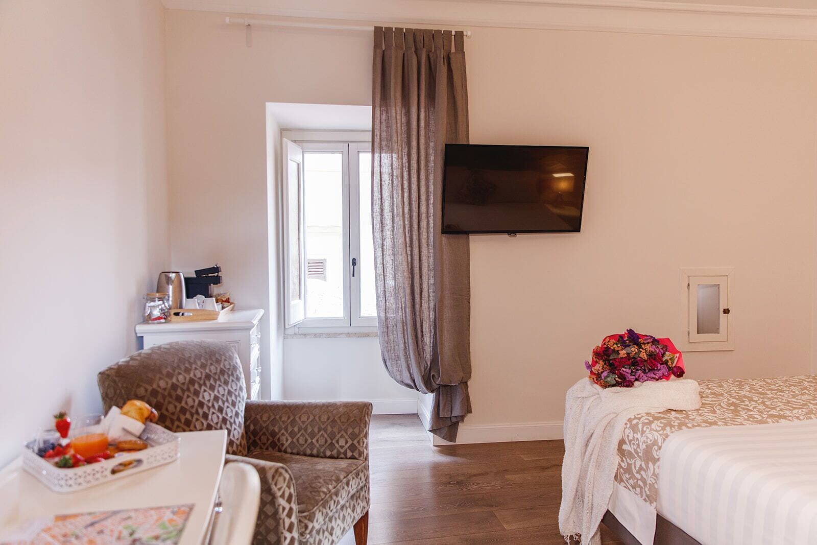 Ein Hotelzimmer mit Bett, Schreibtisch mit Frühstück, Fernseher und einem Fenster mit Vorhängen.