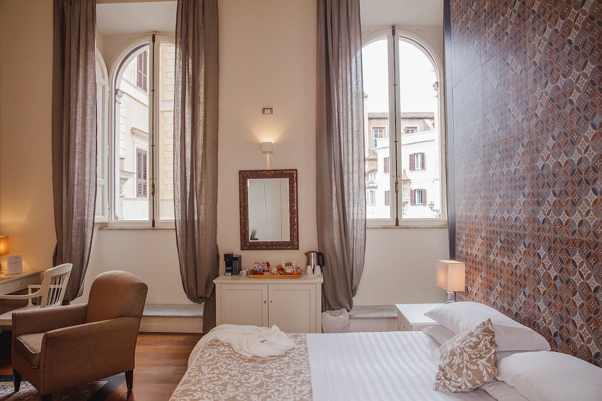 A hotel room with a bed, a chair, a desk, a dresser, and a large window with curtains.