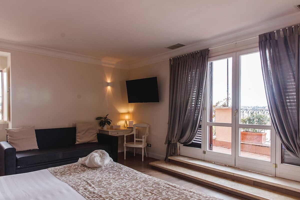 A hotel room with a bed, a desk, a chair, a TV, and a window with curtains.