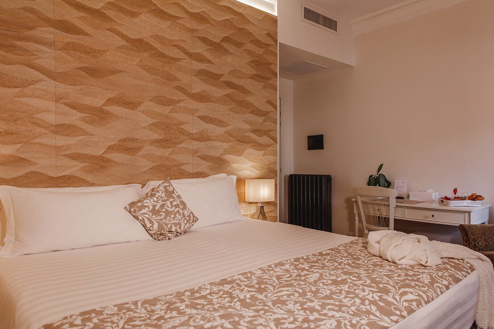 A hotel room with a large bed, a desk, a chair, and a radiator.