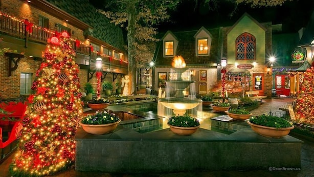 A courtyard with a large Christmas tree, a fountain, and a building with a green facade and a large window. - Smoky Mountain Lodge (Pigeon Forge)