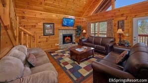 A log cabin interior with a fireplace, leather sofas, a television, and a checkered rug. - Smoky Mountain Lodge (Pigeon Forge)