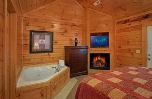 A log cabin room with a wooden interior, a fireplace, a large bed, a TV, and a wooden cabinet. - Smoky Mountain Lodge (Pigeon Forge)