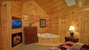 A log cabin bedroom with a fireplace, a television, a framed picture, a bathtub, and a bedside lamp. - Smoky Mountain Lodge (Pigeon Forge)