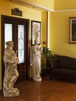 Zona de recepción con una estatua de una mujer sosteniendo una cesta, una estatua de una mujer con un jarrón, y un letrero sobre las puertas que dice "RESTAURANTE".