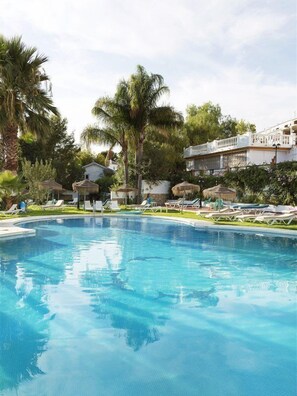 Una piscina con sillones de descanso y palmeras.