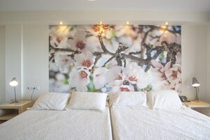 Habitación de hotel con dos camas, un cuadro floral grande en la pared y lámparas de noche.