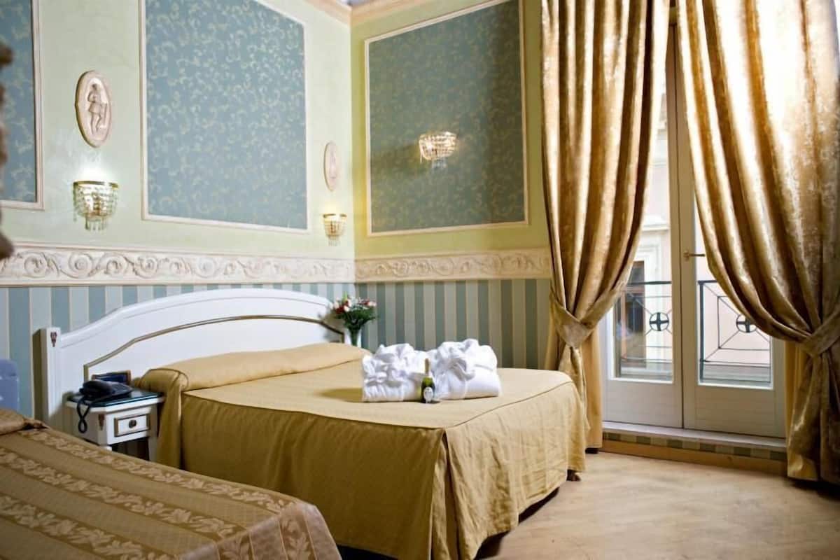 Une chambre d’hôtel avec un lit, une table de chevet, une lampe et une fenêtre avec des rideaux.