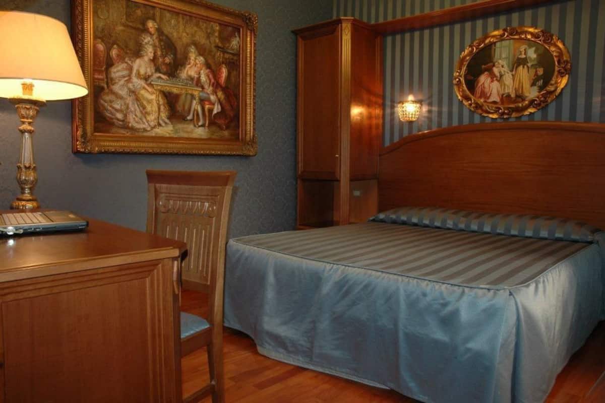 Une chambre à coucher comprenant un lit, un bureau, une chaise, une lampe et deux tableaux encadrés accrochés au mur.