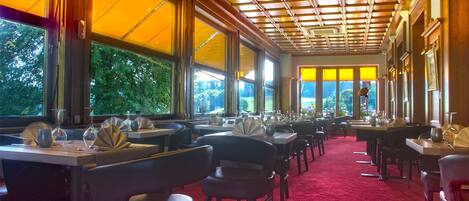 Un restaurante con alfombra roja, techo de madera y amplios ventanales con vistas a la vegetación.