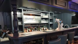 Uma área de bar com prateleiras cheias de garrafas e copos, um balcão e banquetas.