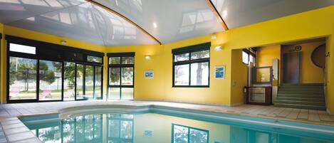 An indoor swimming pool with clear glass walls, yellow walls, and a view of the outdoors.
