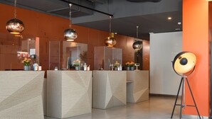 Un área de recepción con mostradores modernos de diseño geométrico, una lámpara de pie y un mostrador de recepción.