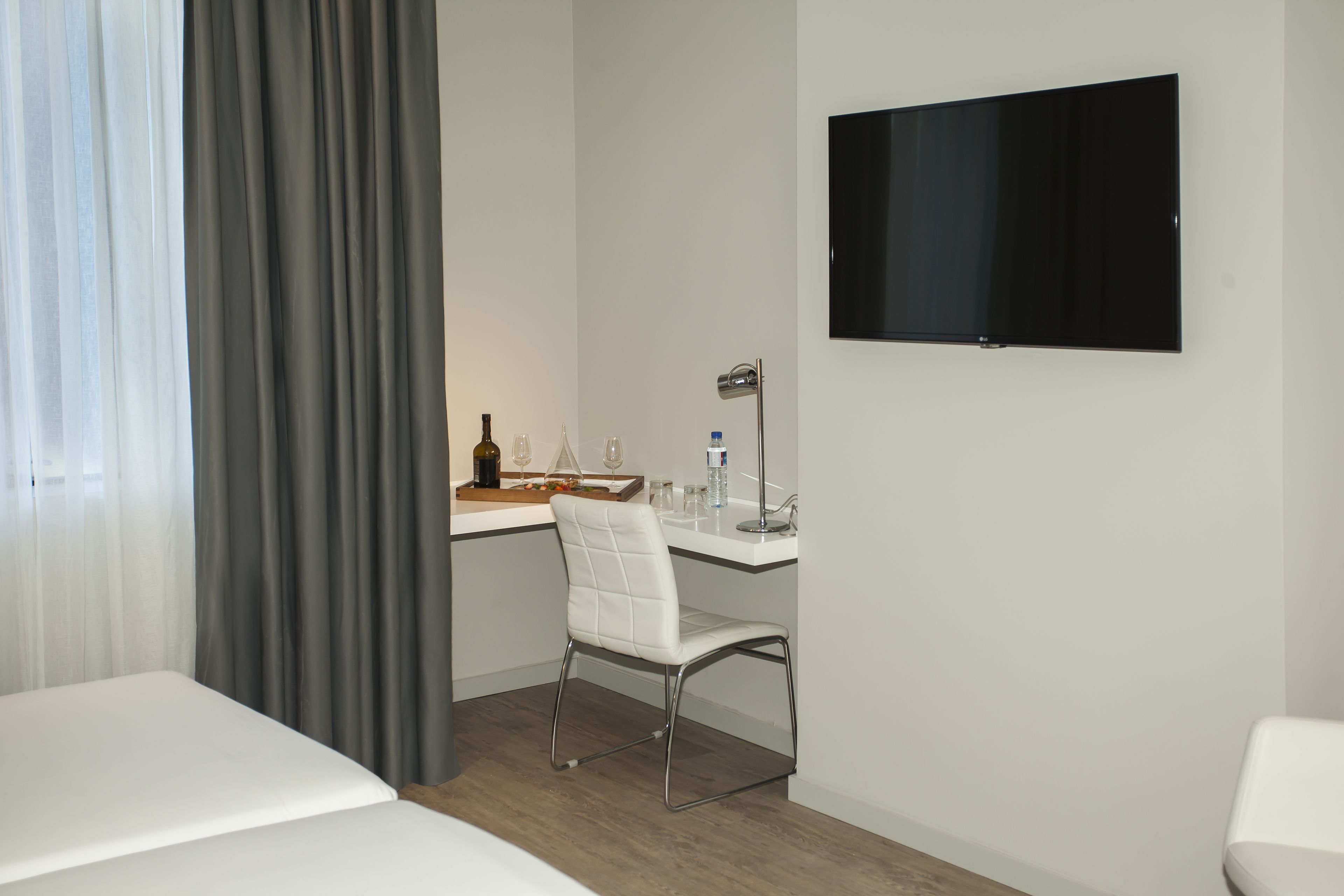 Ein Hotelzimmer mit einem Bett, einem Schreibtisch mit Stuhl, einem Fernseher und einem Fenster mit Vorhängen.