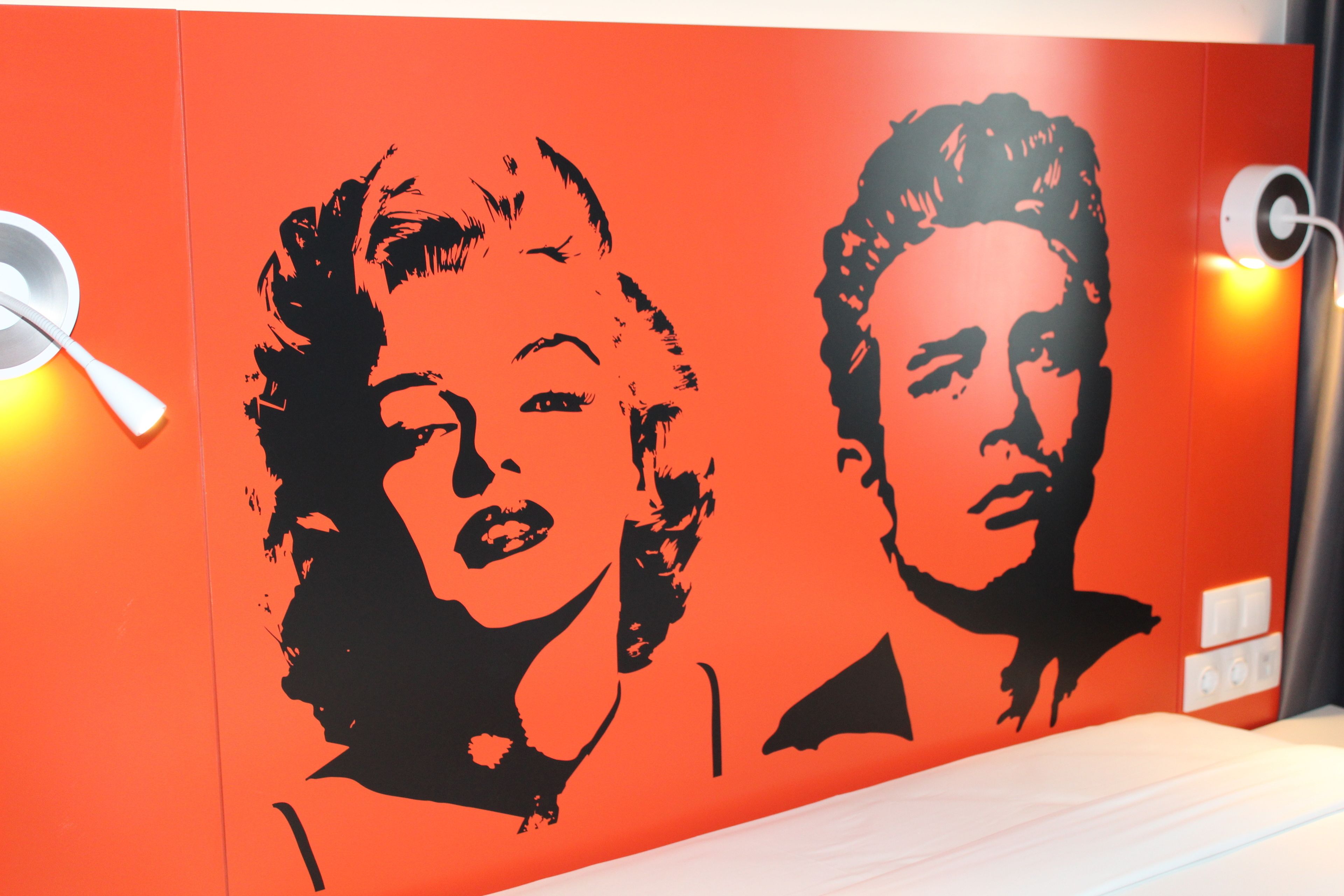 Une pièce dont un mur est peint en rouge et sur lequel figure une grande fresque en noir et blanc représentant deux personnes.