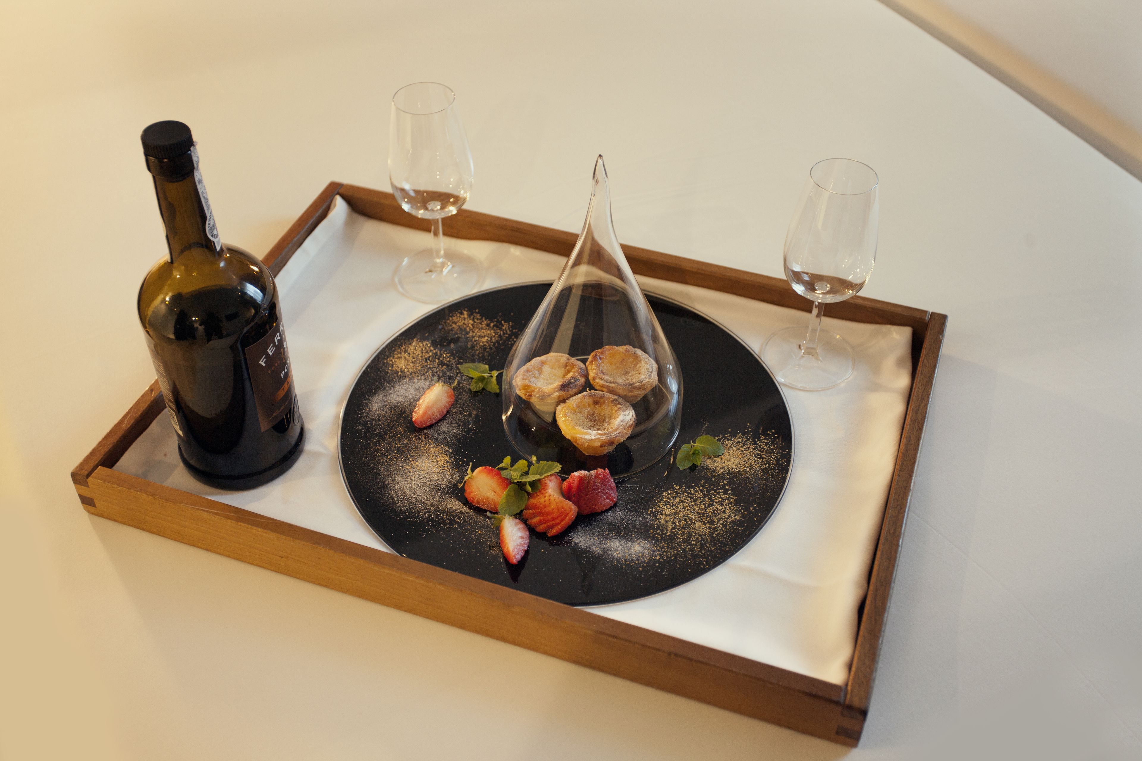 Una bandeja con una botella de vino, dos copas y un plato con pasteles y fresas.