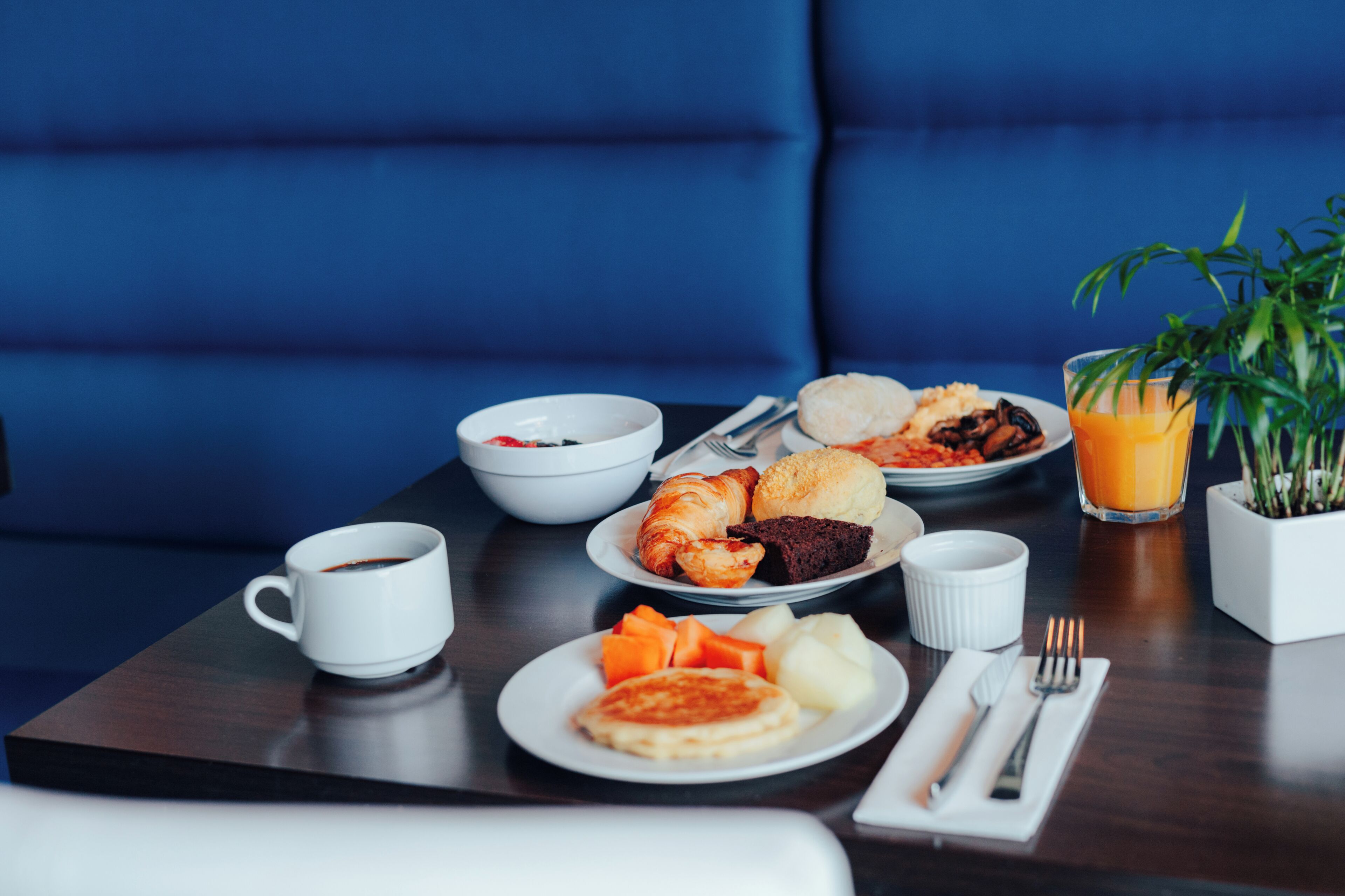 A breakfast table with croissants, muffins, fruit, and a glass of orange juice.