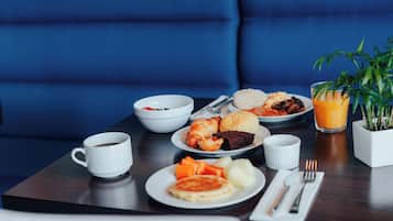 A breakfast table with croissants, muffins, fruit, and a glass of orange juice.