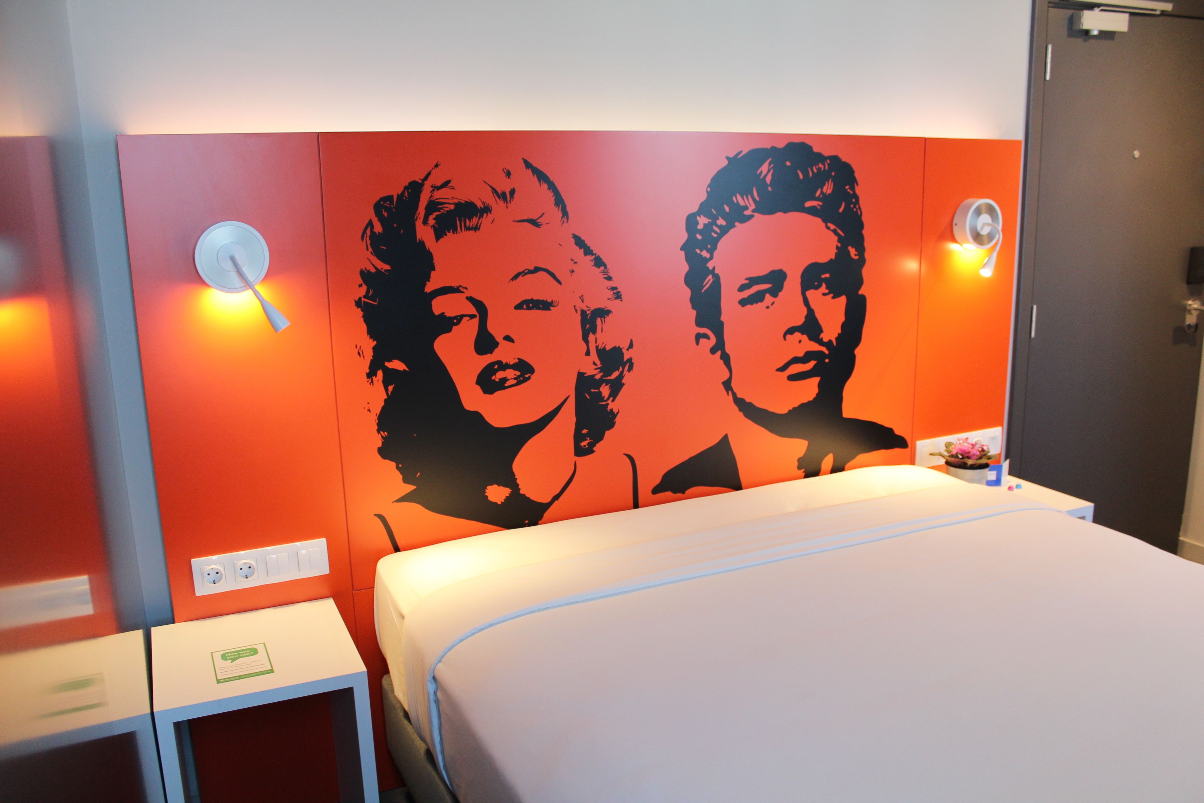 Een hotelkamer met een bed, een wandlamp en een stopcontact.