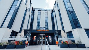 Una entrada de hotel moderna con fachada de vidrio, un llamativo letrero 'Hotel Star Inn' y cielo despejado.