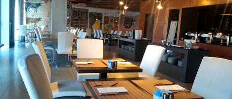 Un restaurant au décor moderne, avec des chaises et des tables blanches, un comptoir où est affiché le menu, et un mur orné d’anciennes affiches.