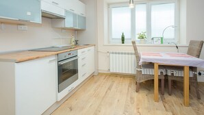 Una cocina moderna con armarios blancos, encimera de madera, horno y un comedor con sillas de mimbre y una mesa.
