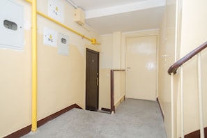A narrow hallway with beige walls, a wooden door, and a yellow pipe running along the wall. - ShortStayPoland Solidarnosci B8 (Warsaw)