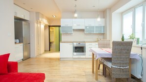 Una cocina moderna con armarios blancos, horno empotrado y un comedor con sillas de mimbre y una mesa.
