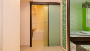 Una habitación con una puerta corredera que da a un baño, una cama frente a una pared verde, y una lámpara colgante.