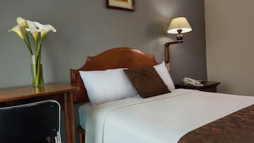 A hotel room with a bed, bedside table, lamp, chair, and a vase with flowers.