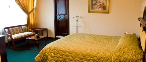 A hotel room with a large bed, a chair, a small table, a door, and a framed picture on the wall.