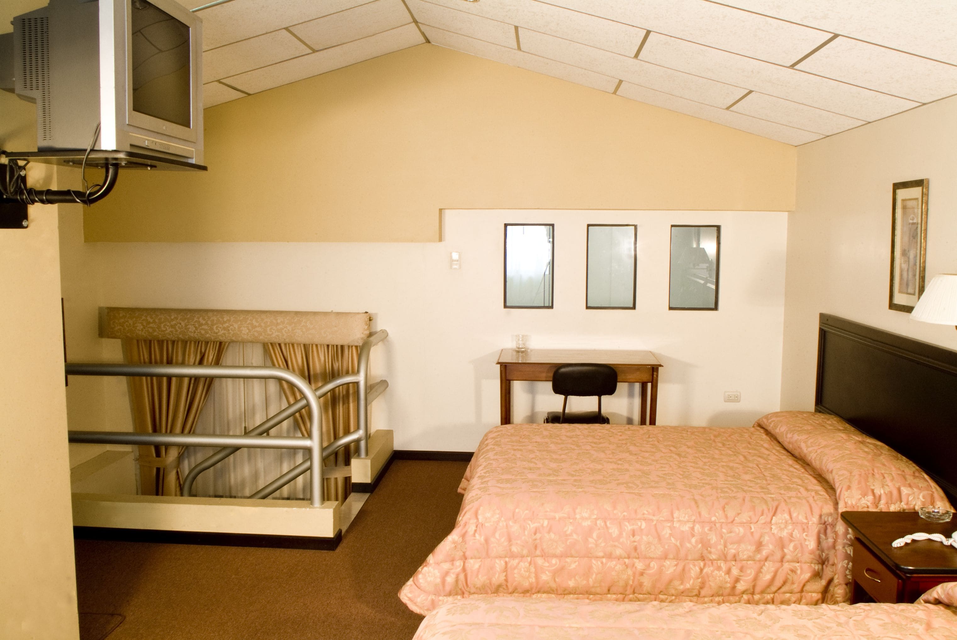 A hotel room with bunk beds, a desk, a chair, a television, and a bed with a headboard.