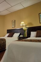 Habitación de hotel con dos camas, una mesita de noche con lámpara, un jarrón con flores y un cuadro en la pared.