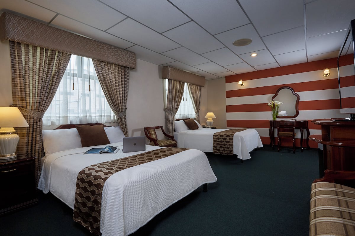 A hotel room with two beds, a desk, a chair, and a television.