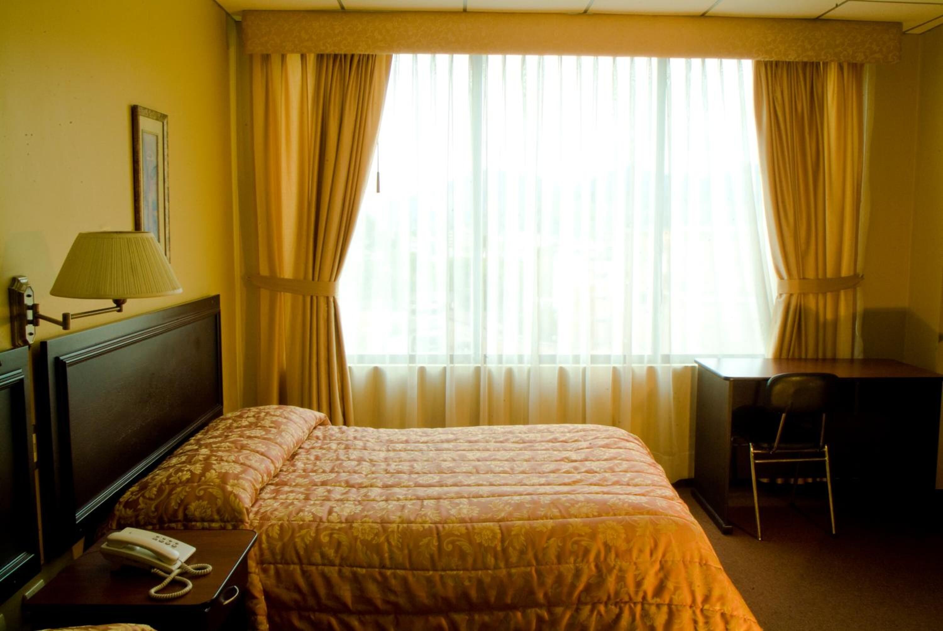 A hotel room with a bed, a desk, a chair, a lamp, and a telephone on the nightstand.